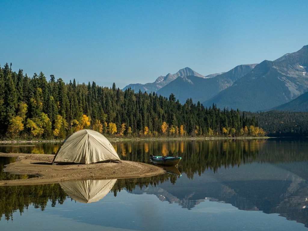 white tent on lake near green trees and mountain under blue sky during daytime